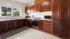 A kitchen with wooden cabinets, a stove, a microwave, and a window with a view of trees. - Best Houses 91 - Casa D'el Rey (Amoreira)