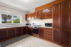 A kitchen with wooden cabinets, a stove, a microwave, and a window with a view of trees. - Best Houses 91 - Casa D'el Rey (Amoreira)