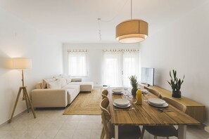 Un moderno salón con una mesa de comedor de madera, un sofá blanco y un gran ventanal con cortinas.