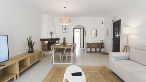 Ein Wohnzimmer mit Fernseher, einer Couch, einem Esstisch mit Stühlen, einem Kamin und einem Flur, der zu einer Tür führt.