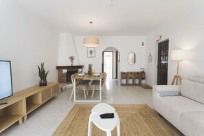 Ein Wohnzimmer mit Fernseher, einer Couch, einem Esstisch mit Stühlen, einem Kamin und einem Flur, der zu einer Tür führt.