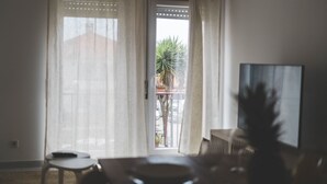 Ein Zimmer mit Blick auf einen Balkon, inklusive Sessel, Tisch und Fernseher.
