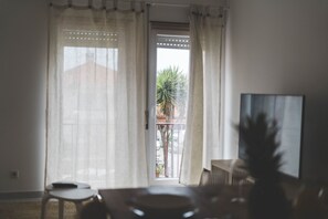Ein Zimmer mit Blick auf einen Balkon, inklusive Sessel, Tisch und Fernseher.