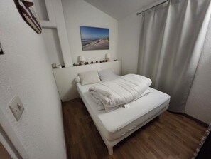 Ein Schlafzimmer mit Bett, Kopfstütze, Wandbild, Nachttisch und einem Fenster mit Vorhängen.