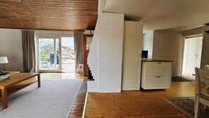 A room with a wooden floor, a white brick wall, a wooden table, and a small white cabinet. - Archipelago House by the Bohuslän Cliffs | SE09181 (Hjälteby)