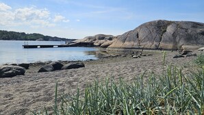 Una costa rocosa amb un moll que s'endinsa en aigües tranquil·les, envoltada d'una vegetació escassa i turons allunyats.
