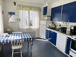 A kitchen with a checkered table, white chairs, blue cabinets, a window with curtains, and a hanging light fixture. - Charming archipelago house in Grebbestad | SE09082 (Grebbestad)