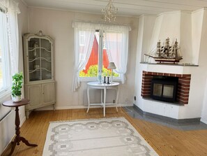 Una habitació amb una xemeneia, una taula amb una làmpada, un armari i una finestra amb cortines.