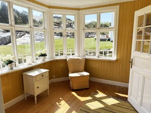 A corner room with a bay window, a white dresser, a cushioned chair, and a wooden floor. - Charming archipelago house in Grebbestad | SE09082 (Grebbestad)
