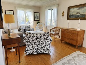 A room with a wooden floor, a sofa, a dining table, a wicker chair, a wooden cabinet, and a painting on the wall. - Charming archipelago house in Grebbestad | SE09082 (Grebbestad)