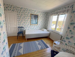 A bedroom with a bed, a chair, a window with curtains, a door, and a patterned wall. - Charming archipelago house in Grebbestad | SE09082 (Grebbestad)