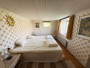 Habitació amb un llit, una cadira, un escriptori amb una làmpada, una finestra amb cortines i una paret amb una decoració solar.