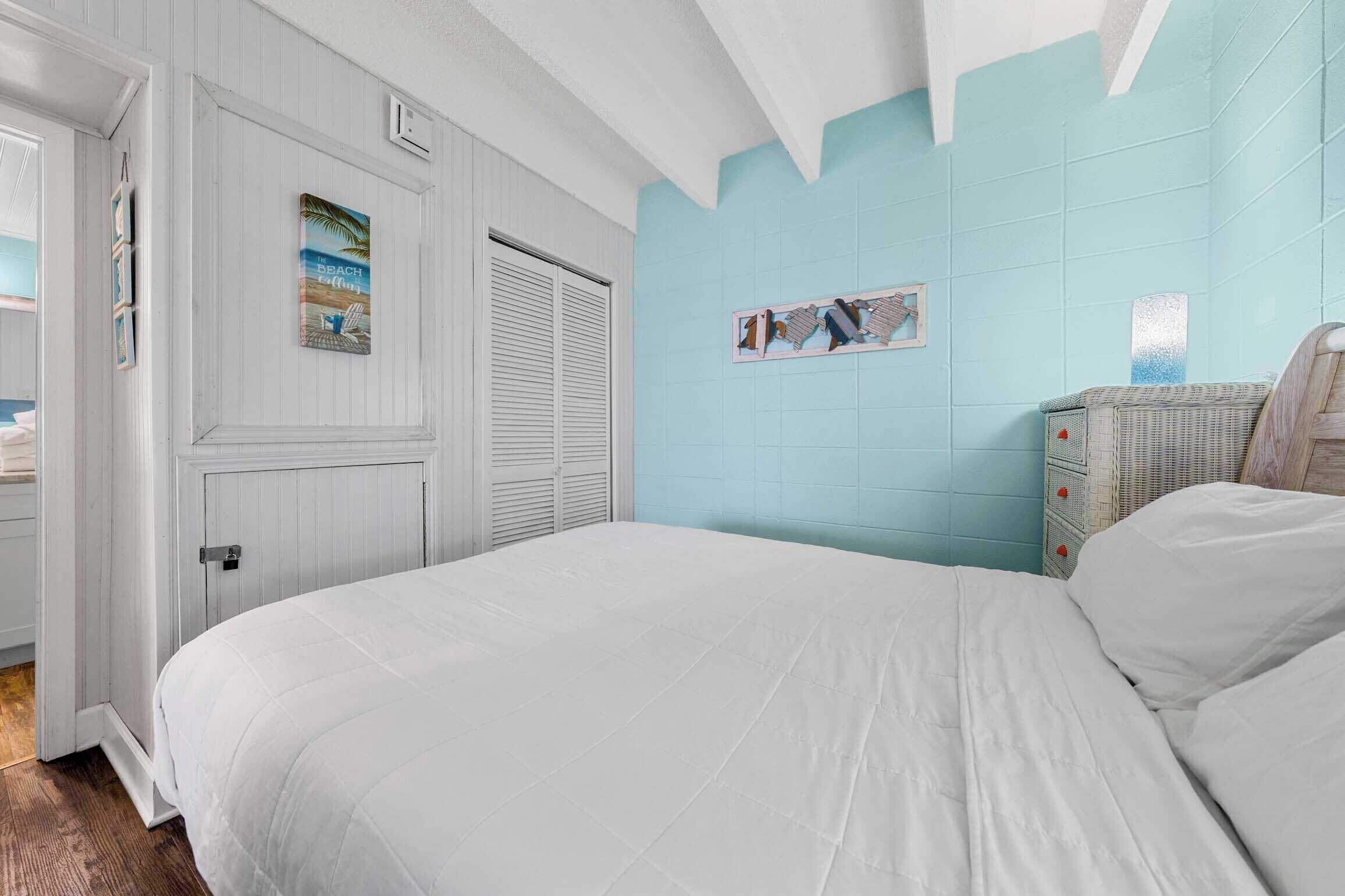 A bedroom with a bed, a wardrobe, and a wall with a beach-themed picture.
