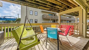 Una terraza de madera con un columpio, sillas y una mesa.