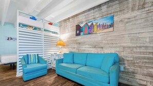 Una habitación con un sofá azul, un sillón a rayas, una pared de madera y un cuadro colorido.