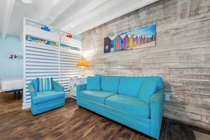 Une pièce avec un canapé bleu, un fauteuil à rayures, un mur en bois et un tableau coloré.
