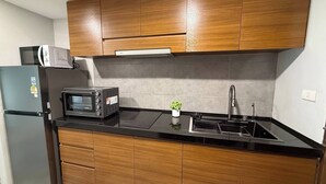A compact kitchen with wooden cabinets, a black countertop, a built-in microwave, a toaster, and a stainless steel sink. - Stylish Loft Apartment Near Fishermans Village (Koh Samui)