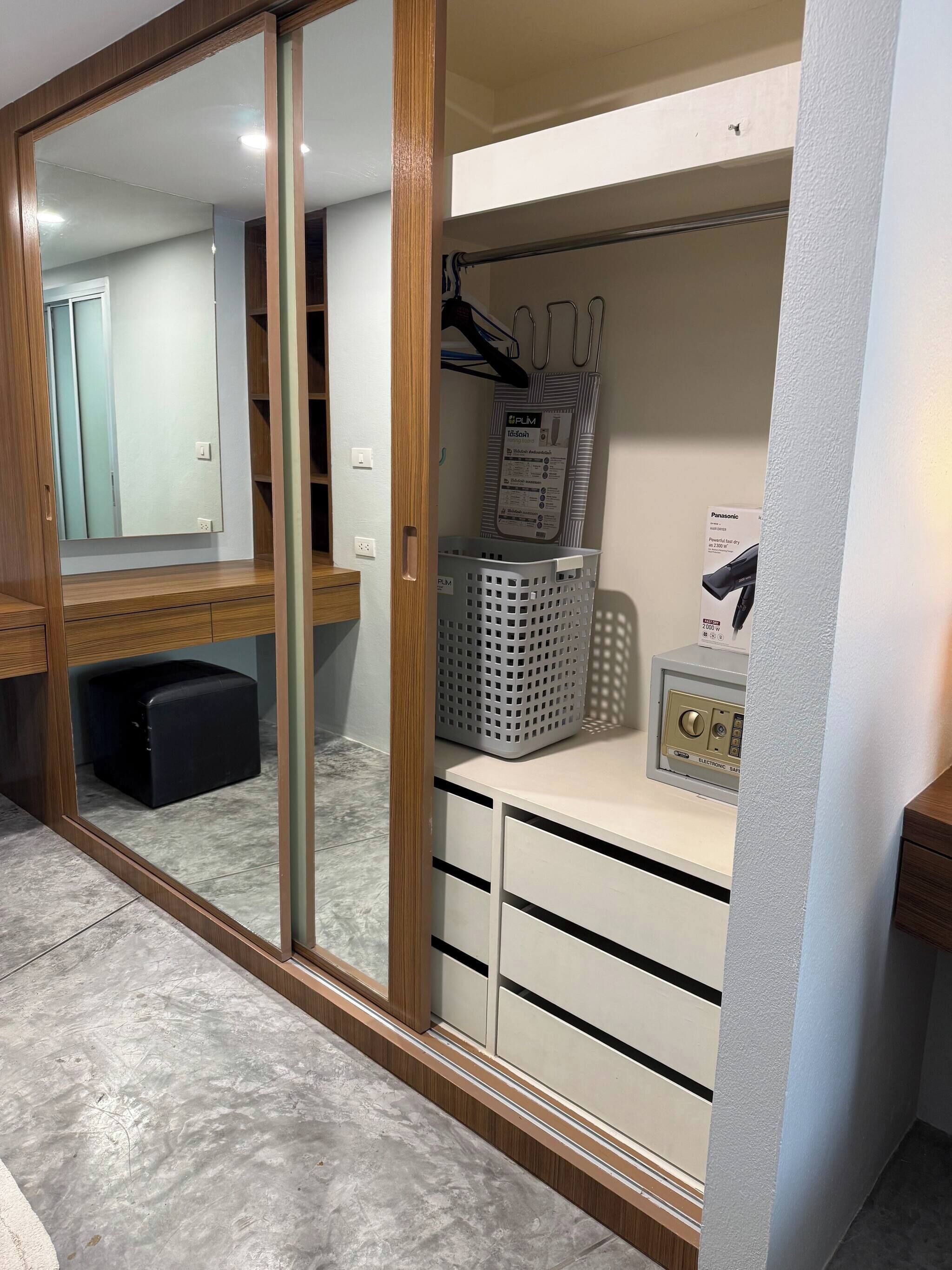 Ein Zimmer mit einem Holzschrank, einem Spiegel, einem Wäschekorb und einem Panasonic-Gerät.