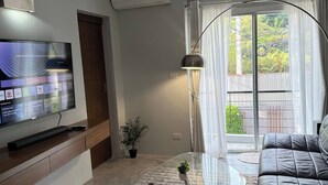 A modern living room with a flat-screen TV, a glass coffee table, a leather sofa, and a view of the outdoors through a large window. - Stylish Loft Apartment Near Fishermans Village (Koh Samui)