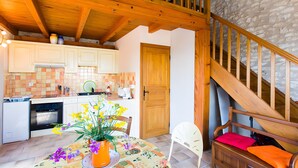 A kitchen with wooden beams, a dining table with a floral tablecloth, a white chair, and a wooden bench with cushions. - Holiday Home "La Cabane du Vigneron" with Shared Pool, Private Terrace & Air Conditioning (Donnazac)