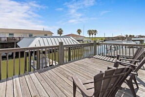 Eine Holzterrasse mit Stühlen, Blick auf Wasser und Gebäude im Hintergrund.