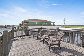 Eine Holzterrasse mit Adirondack-Stühlen, ein Gebäude mit Gründach und Blick auf das Wasser.