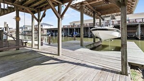 A wooden dock with a boat, a covered area with wooden beams, and a building in the background. - RV with AC on Bolivar Peninsula (Bolivar Peninsula)