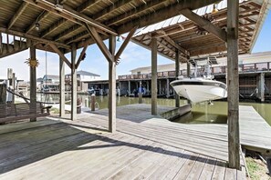 Eine Holzsteg mit einem Boot, ein überdachter Bereich mit Holzbalken und ein Gebäude im Hintergrund.