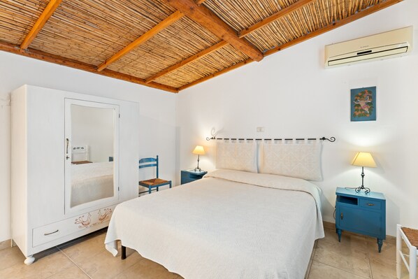 A bedroom with a bed, wardrobe, two bedside tables with lamps, a ceiling fan, and a wall-mounted air conditioner.
