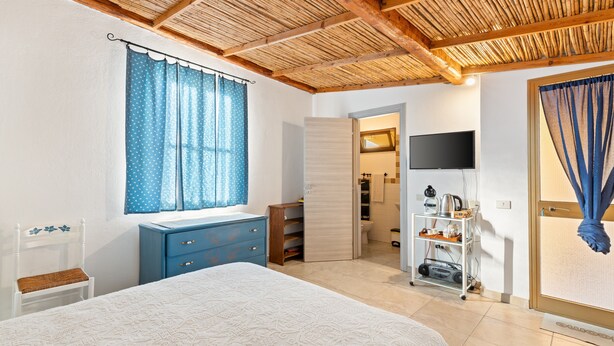 Un dormitorio con cama, cómoda, televisor y baño visible a través de una puerta abierta.