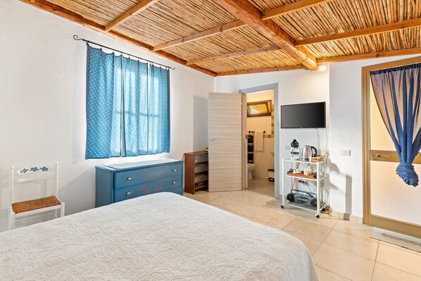 A bedroom with a bed, a dresser, a television, and a bathroom visible through an open door. - Guest House 'Suite Simone' with Shared Garden and Air Conditioning (Pranixeddu)
