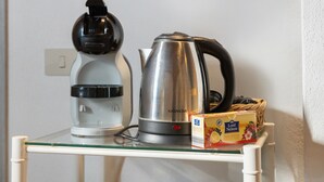 Una cocina con cafetera, hervidor y una caja de té de frutas sobre una repisa de vidrio.
