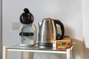 A kitchen area with a coffee maker, a kettle, and a box of fruit tea on a glass shelf.