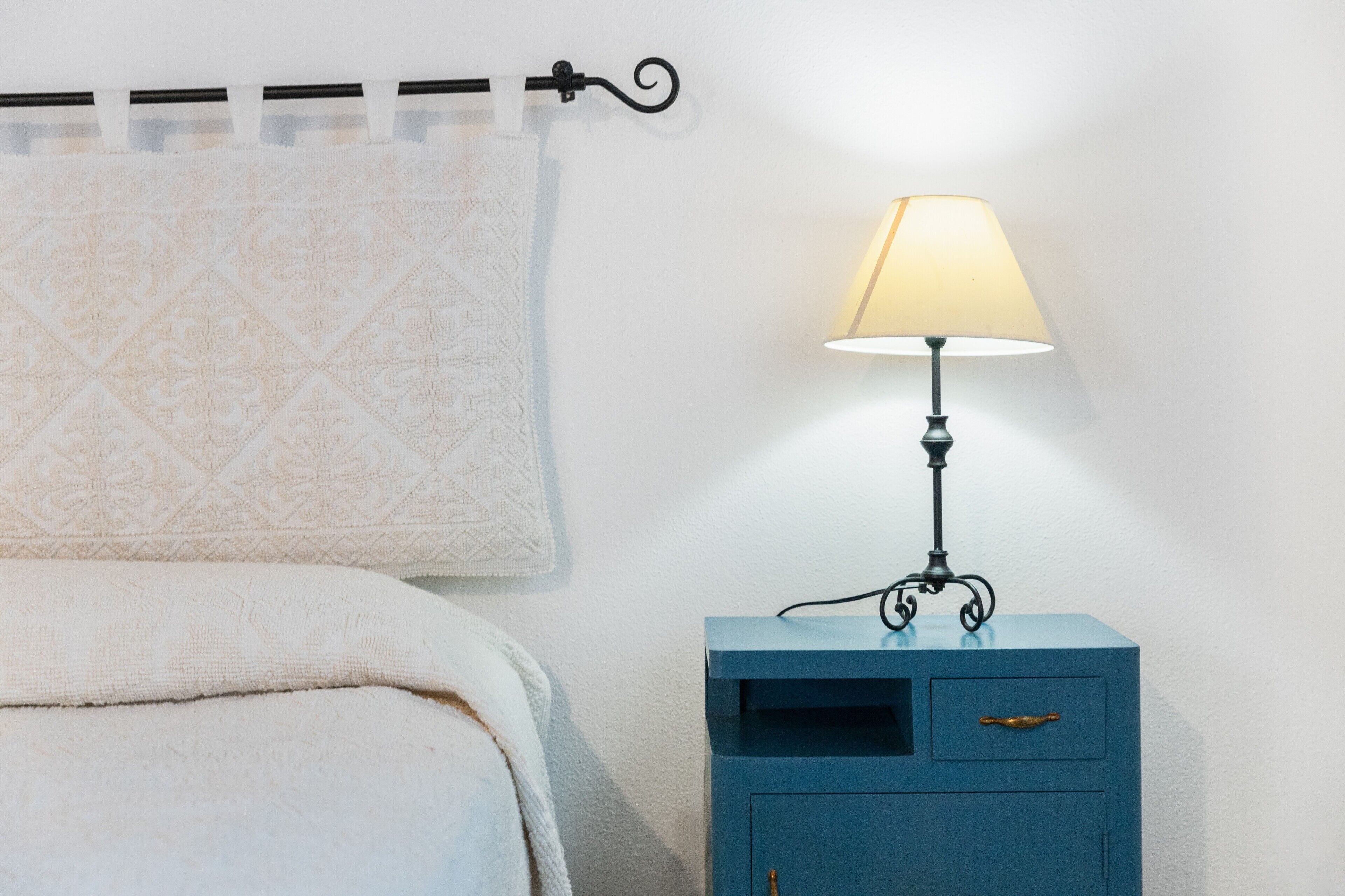 A bed with a patterned blanket, a bedside lamp, and a small blue nightstand with a drawer.