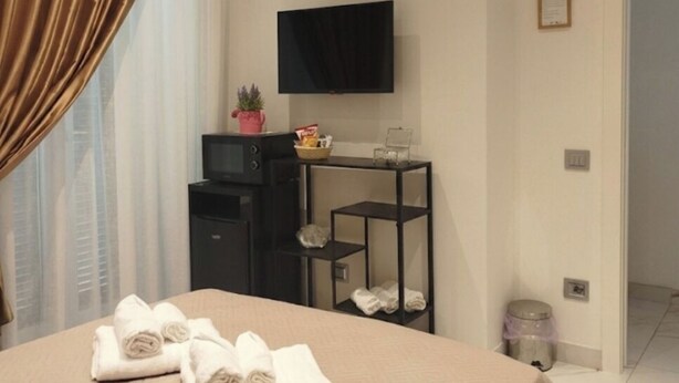 A hotel room with a bed, a TV, a desk with a chair, and a window with curtains. - Domus Costa - Positano (Cava de' Tirreni)
