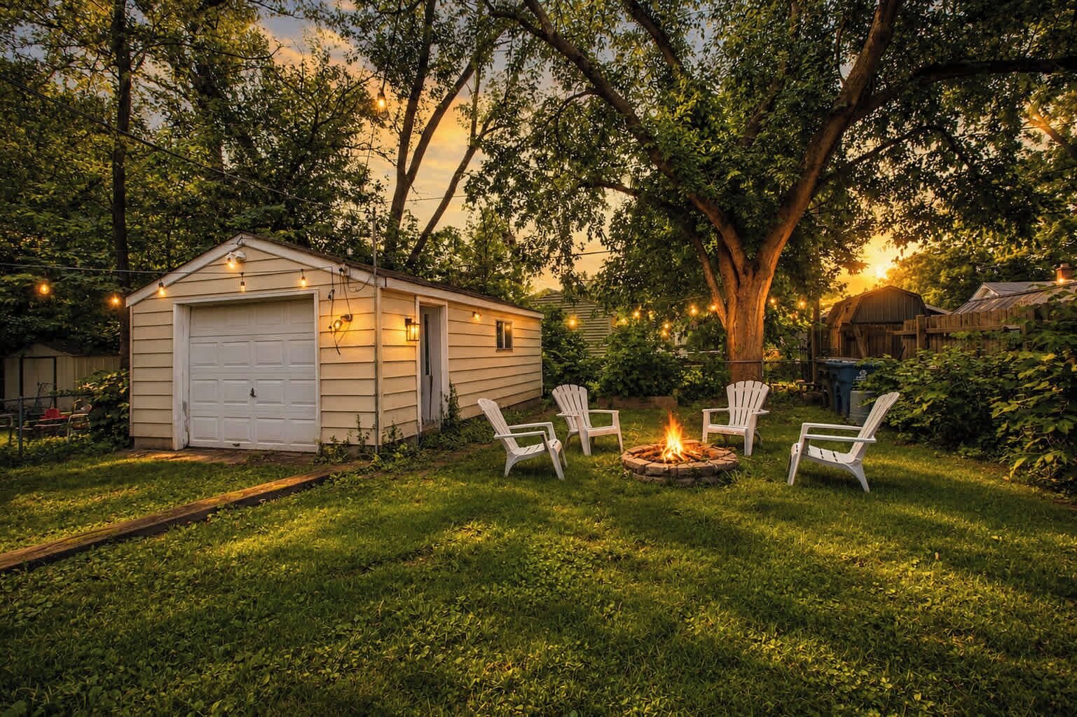 A backyard with a fire pit, white chairs, and a shed.