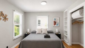 Ein Schlafzimmer mit einem Bett, zwei Nachttischen, einem Kleiderschrank und einem Fenster mit Jalousien.