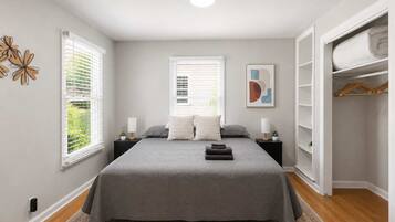 Une chambre à coucher comprenant un lit, deux tables de chevet, une commode, une armoire et une fenêtre avec des stores.
