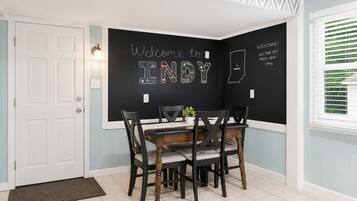 Un coin repas avec un mur recouvert d’un tableau noir, une porte blanche et une fenêtre avec des stores.
