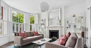 Ein Wohnzimmer mit beiger Couch, Couchtisch, Kamin und weißen Regalen.
