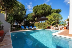 A swimming pool with lounge chairs and umbrellas, surrounded by trees and greenery. - Holiday Home 'Guatemala' with Private Pool, Wi-Fi and Air Conditioning (Quarteira)