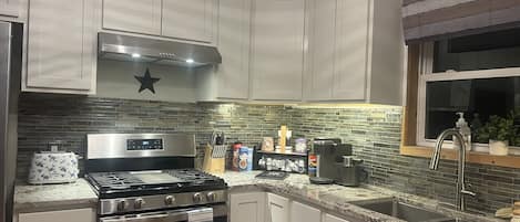 A kitchen with white cabinets, a stainless steel stove, a microwave, and a window with a view.