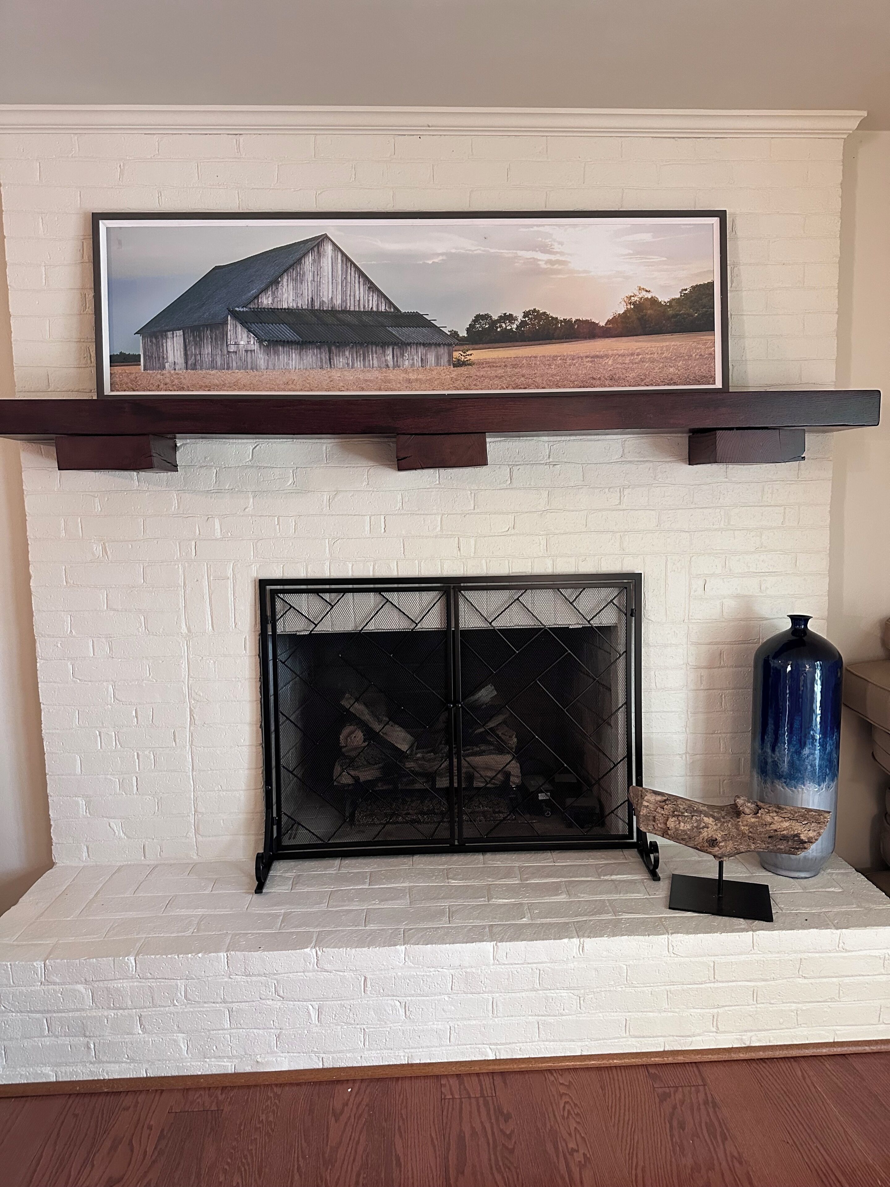A fireplace with a white brick surround, a mantel with a framed picture, and a blue vase on the right.
