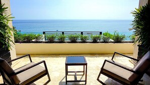 A balcony with two wicker chairs and a small table, overlooking a calm sea.