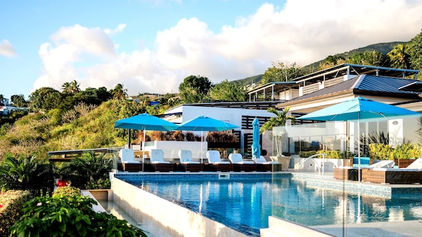 A swimming pool with lounge chairs and umbrellas, surrounded by greenery and a hillside.