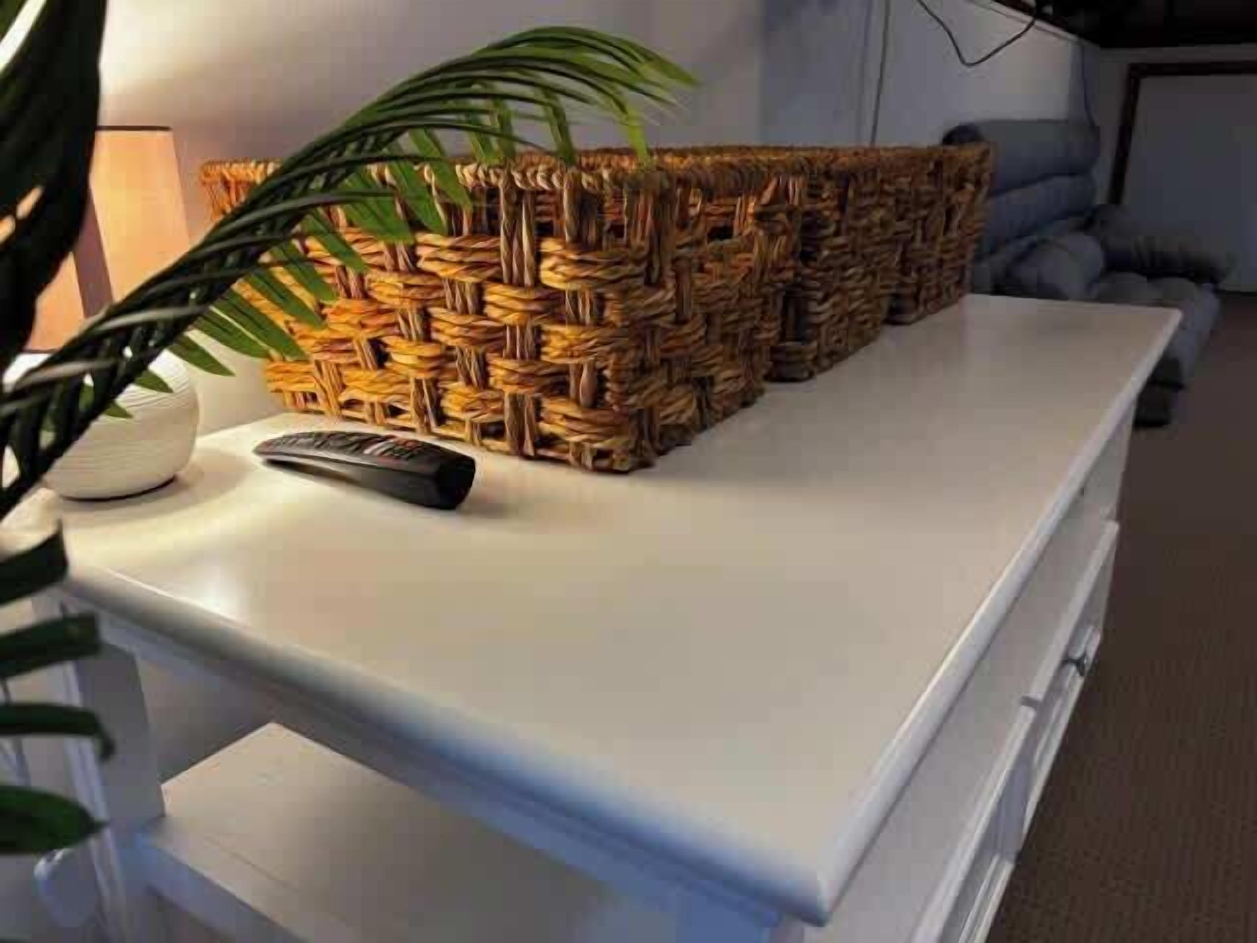 A white table with a woven basket and a remote control.