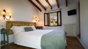 Een slaapkamer met een bed, twee nachtkastjes, een raam met gordijnen, een aan de muur bevestigde televisie en een radiator.