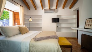 Un dormitori amb llit, una làmpada de nit, televisió i una petita banca.