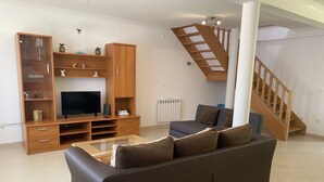 Ein Wohnzimmer mit Sofa, Fernseher, Holz-Multimöbel und einer Treppe.
