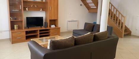 A living room with a sofa, TV, wooden entertainment unit, and a staircase.